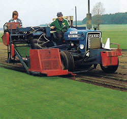 Med stora moderna maskiner skördas den färdiga gräsmattan. Två man betjänar maskinen.