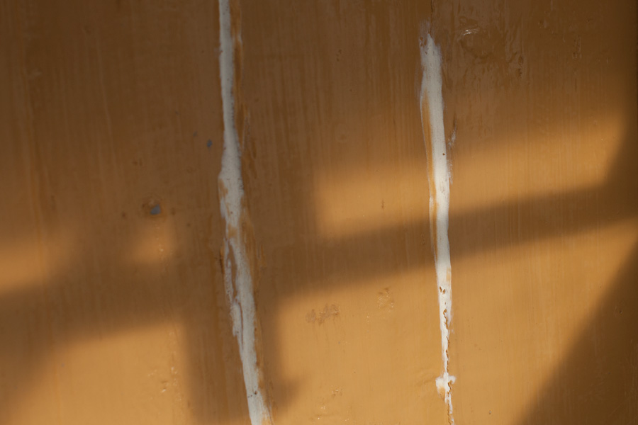 En närbild på en träfasad som visar ifyllda sprickor med fönsterkitt som förhindrar att slagregn kan tränga in i fasadsprickor.